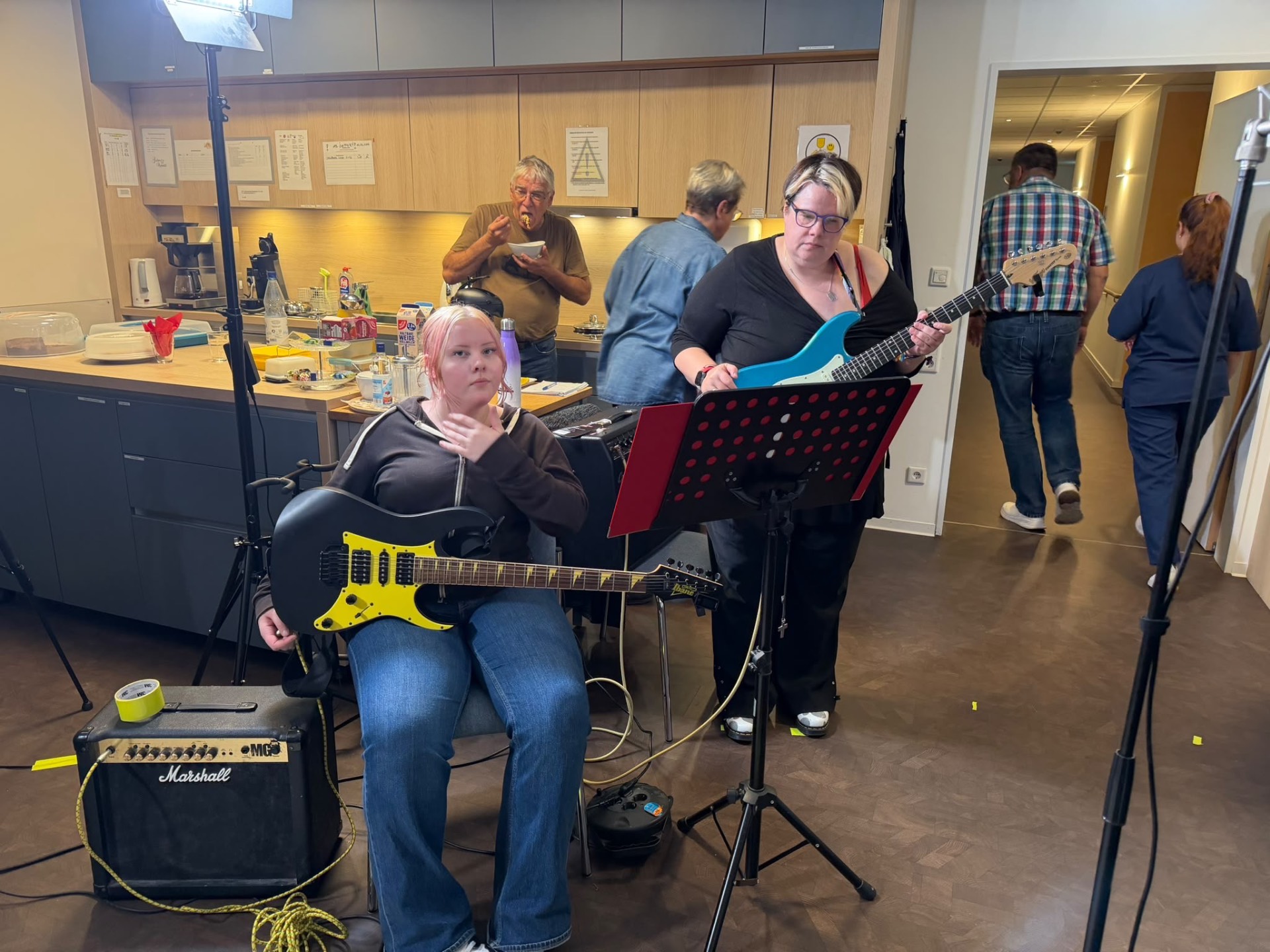 Hinter den Kulissen des Livestreamkonzerts: Zwei Musikerinnen mit E-Gitarren an Verstärker und Notenpult, im Hintergrund die Küche.